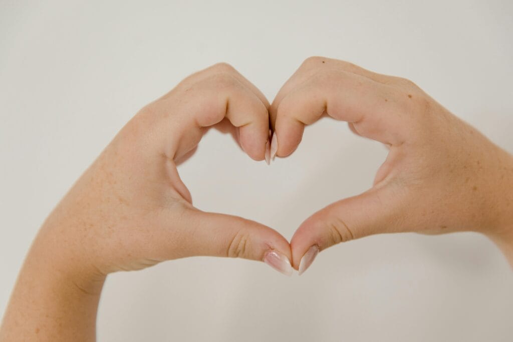 Close-up of hands making a heart shape on a neutral background, symbolizing love and connection.