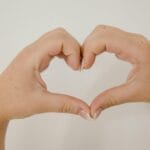 Close-up of hands making a heart shape on a neutral background, symbolizing love and connection.