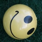 Close-up of a yellow smiley face ball resting on green grass.