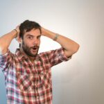 A surprised man with a beard, holding his head in astonishment in a studio setting.