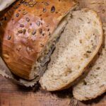 Close-up of sliced brown seeded bread on a rustic wooden cutting board with a paper bag.