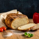 Delicious freshly baked sourdough bread with tomatoes and pepper on a rustic wooden table.