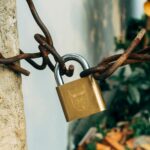 A brass padlock securing a rusty wire on a concrete post, symbolizing security and protection.