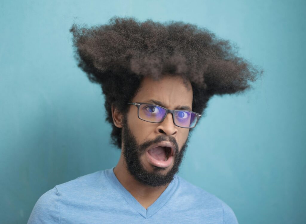 Portrait of a surprised man with afro hair and glasses on a blue background.