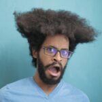 Portrait of a surprised man with afro hair and glasses on a blue background.