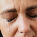 Emotional close-up of a woman's face with closed eyes and tears expressing distress.