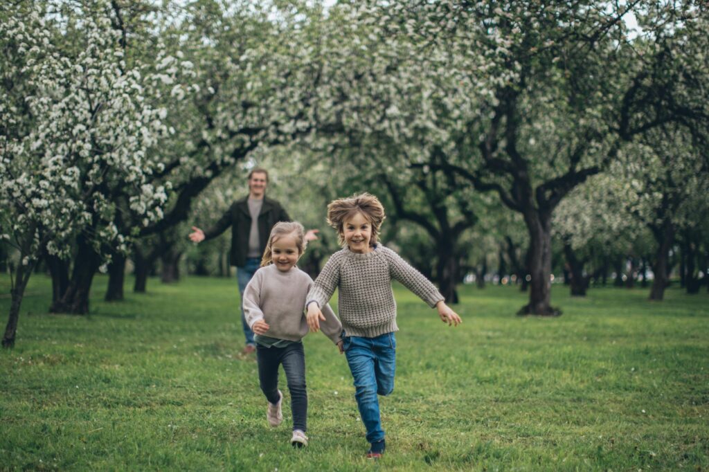 A cheerful father and two children running through a blossoming park, enjoying springtime together.