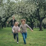 A cheerful father and two children running through a blossoming park, enjoying springtime together.