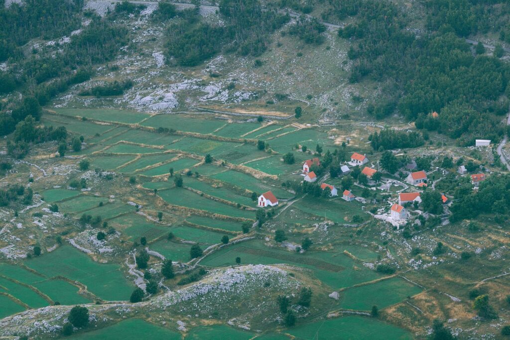 Aerial perspective showcasing rural farmland and a quaint village with red-roofed houses surrounded by fields and hills.