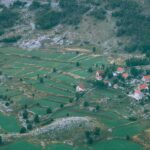 Aerial perspective showcasing rural farmland and a quaint village with red-roofed houses surrounded by fields and hills.