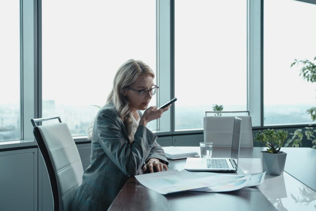 Businesswoman using phone in modern office with laptop and documents.