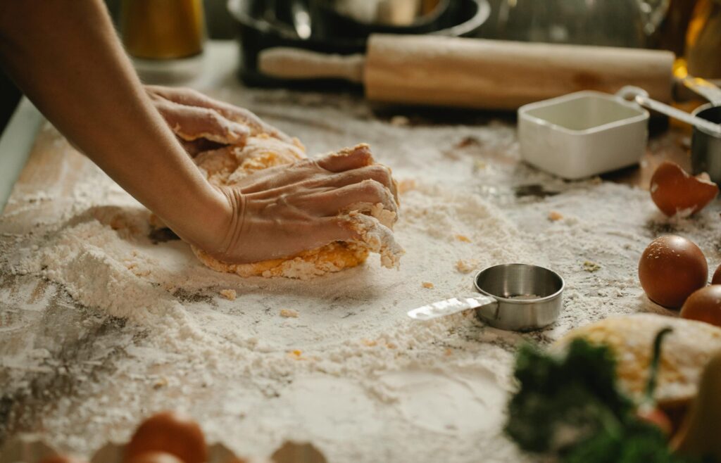 A baker's hands knead dough on a floured kitchen table surrounded by ingredients.