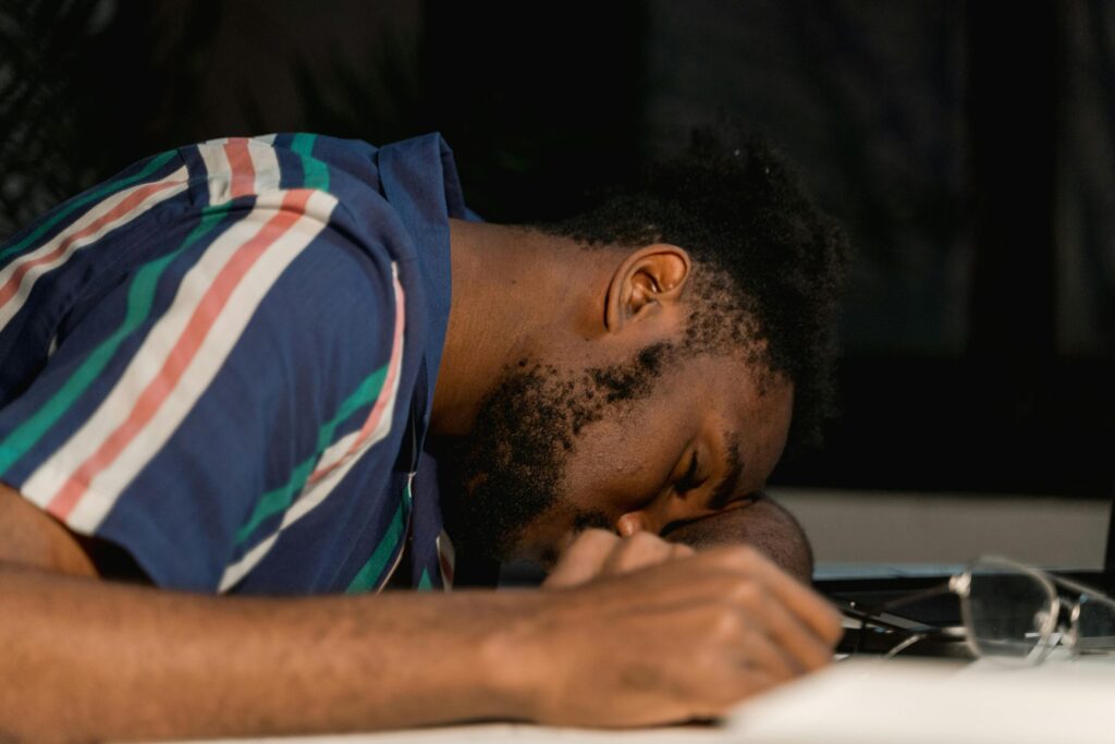 A man with facial hair rests his head on a desk, napping during a late work session.