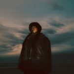 A person stands on a beach under a cloudy sky.