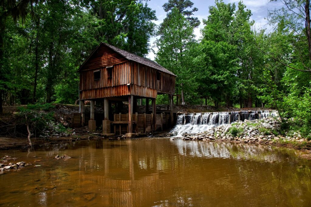Historic wooden mill by a serene waterfall, surrounded by lush green forest.