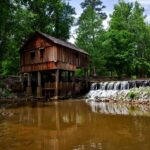 Historic wooden mill by a serene waterfall, surrounded by lush green forest.