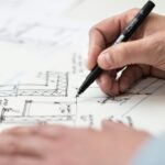 Close-up of hand drawing intricate technical designs on blueprint with pen, ideal for engineering or architecture themes.