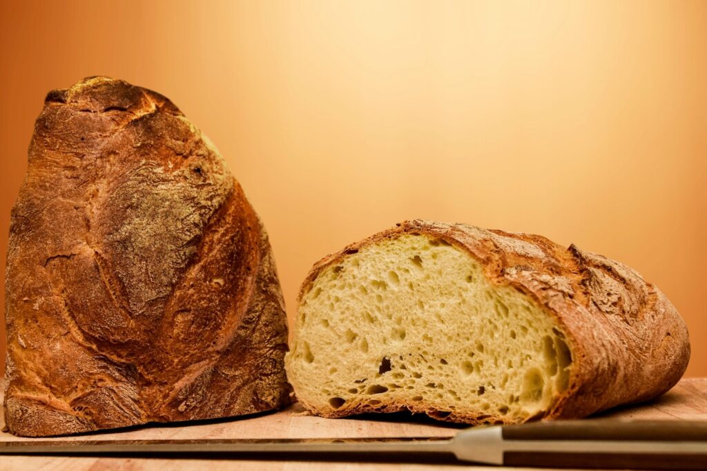Close-up of a rustic artisan bread loaf, half sliced, with a knife on a wooden table.