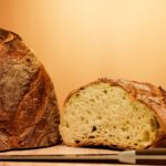 Close-up of a rustic artisan bread loaf, half sliced, with a knife on a wooden table.