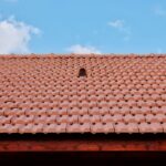 A detailed view of a red tiled roof with vent against a clear blue sky, showcasing architectural design.