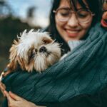 A joyful couple cuddles their Shih Tzu in a cozy blanket during a delightful day outdoors.