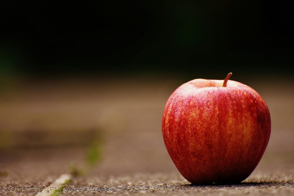 Close-up of a fresh red apple on a rustic background with blurred foreground.