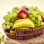 A colorful wicker basket filled with fresh grapes, bananas, and apples on a wooden table.