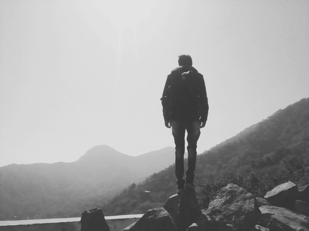 A lone hiker stands on rocks, overlooking misty mountain landscape, capturing the essence of adventure.