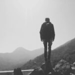 A lone hiker stands on rocks, overlooking misty mountain landscape, capturing the essence of adventure.
