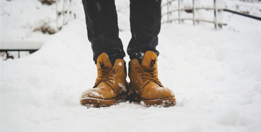 Feet in yellow boots standing on fresh snow, showcasing winter fashion.