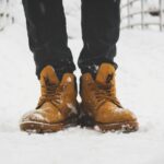 Feet in yellow boots standing on fresh snow, showcasing winter fashion.
