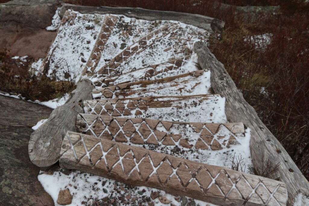 Wooden stairs with geometric patterns dusted in snow on a hiking trail.