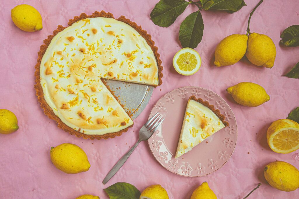 Top view of a lemon tart with fresh lemons on a pink background, perfect for dessert inspiration.