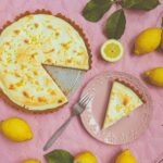 Top view of a lemon tart with fresh lemons on a pink background, perfect for dessert inspiration.