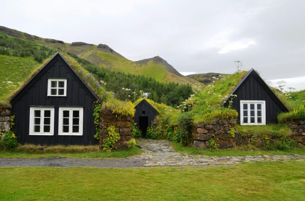 Explore the rustic charm of traditional turf roofed houses set against a lush hillside in serene countryside.