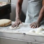 A baker in an indoor kitchen kneading dough for bread preparation, showcasing traditional baking techniques.