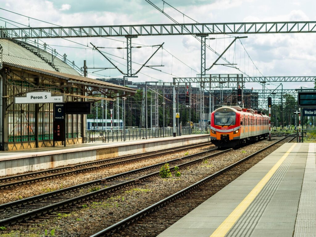 Orange train at an empty station platform with overhead wires.
