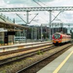 Orange train at an empty station platform with overhead wires.