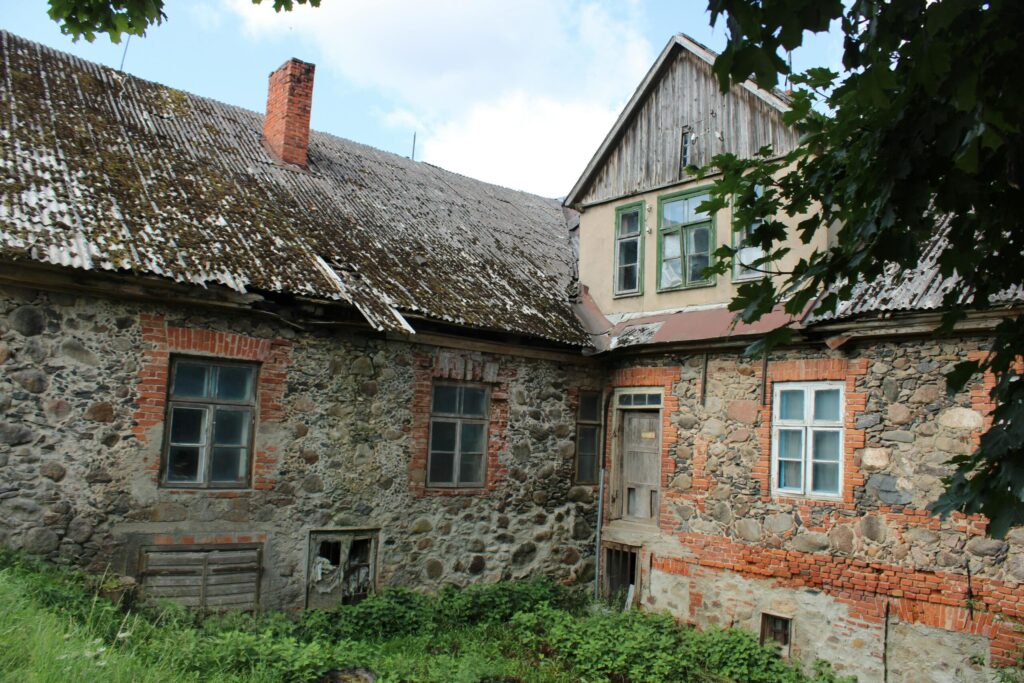 Charming old stone house with a weathered roof surrounded by greenery, epitomizing rustic architecture.