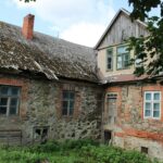 Charming old stone house with a weathered roof surrounded by greenery, epitomizing rustic architecture.