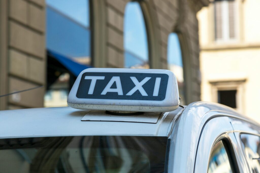 Close-up view of a taxi sign atop a vehicle on an urban city street with blurred architectural background.