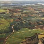 An aerial view showcasing rolling hills and lush farmland under a clear sky.
