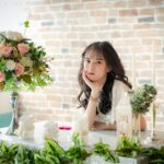 A woman elegantly posing at a table adorned with flowers and candles.