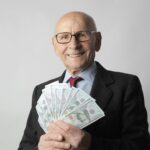 Senior man in a suit with glasses holding US dollars, symbolizing wealth and savings.