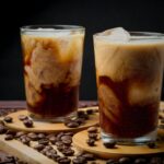 Delicious iced coffee with swirling cream served in glass cups surrounded by coffee beans.