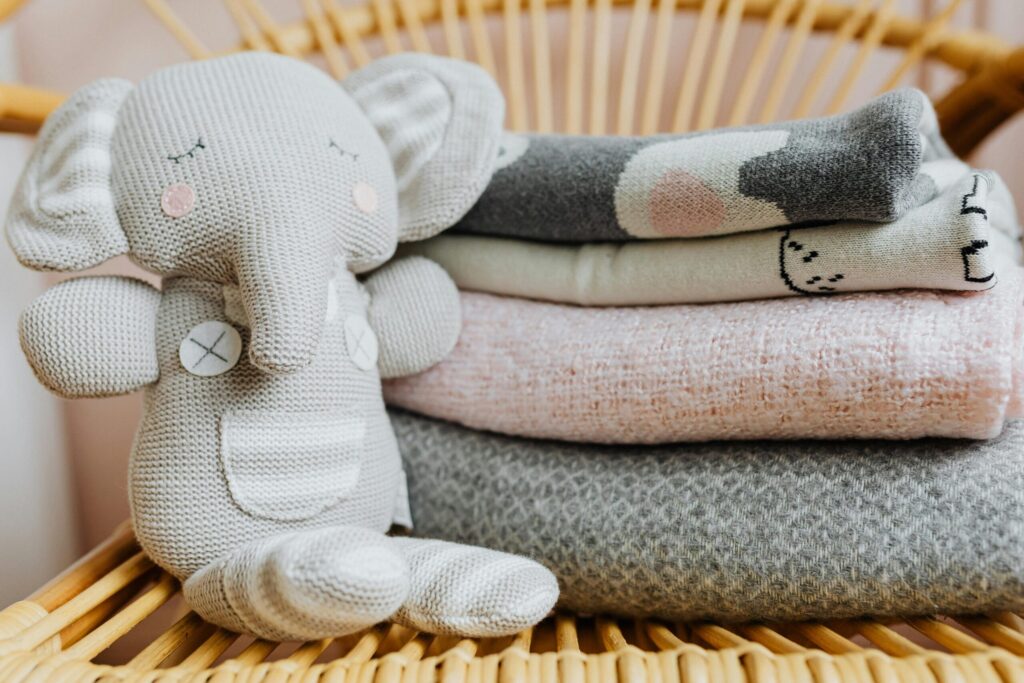 Cute knitted elephant toy and pastel blankets on a wicker chair, perfect for a cozy nursery.