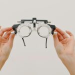 Crop unrecognizable female demonstrating modern trial frame with optical lenses against white background in optometrist studio