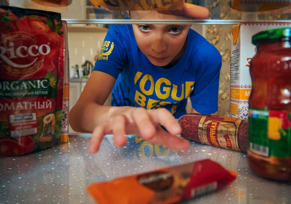 Young boy reaching into refrigerator for a snack. Close-up view indoors.