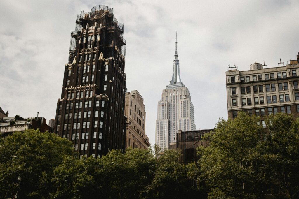 From below of famous American standard building placed near Empire state building on street with green bushes on Manhattan In New York