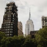 From below of famous American standard building placed near Empire state building on street with green bushes on Manhattan In New York